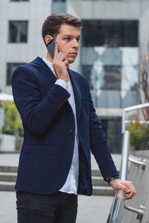 Business style. A young businessman is talking on the phone from the street. The guy in the blue jacketの写真素材