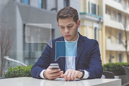 Businessman holds phone in his hand. The guy is sitting at a table on the terrace in a cafe.の写真素材