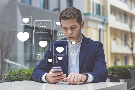 Businessman holds phone in his hand. The guy is sitting at a table on the terrace in a cafe.の写真素材