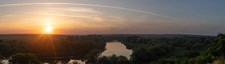 Sunset on the horizon. Panoramic shot. A winding river surrounded by green treesの写真素材