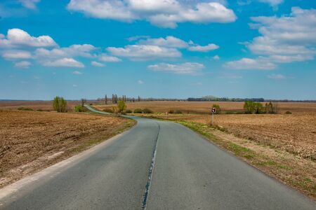 Deserted road. Clear blue sky with white clouds. Winding roadの写真素材