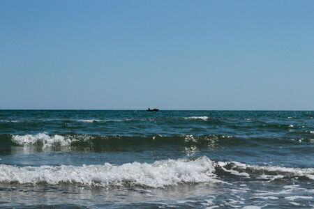 Silhouette of a fisherman on a boat in the sea. Small waves at sea. Clear sky over the horizonの写真素材