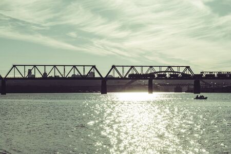Kiev, Ukraine - January 2020. Railway bridge. A freight train is traveling along the bridge. A boat with fishermen on the riverのeditorial素材