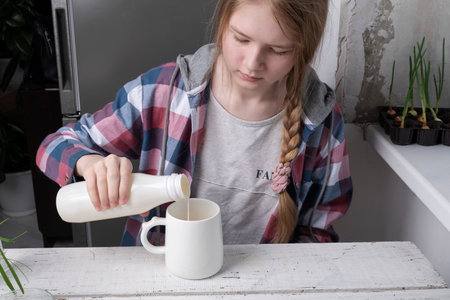 girl pours milk into a mug. Healthy lifestyle concept.の写真素材