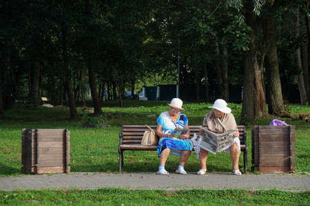 Two elderly women in the park read newspapersの写真素材