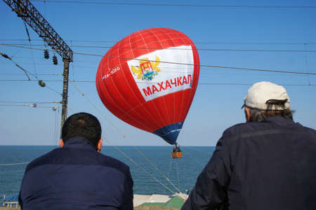 Men on the embankment watch a red hot air balloon with the inscription Makhachkalaの写真素材