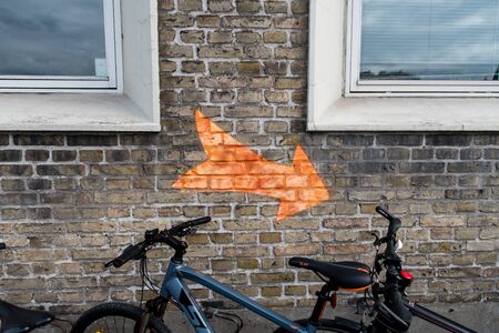 Orange arrow on the wall bettween two windows and a bikeの写真素材