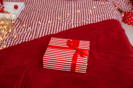 xmas Gift with ribbon lies on bed Close Up. Christmas present packed in kraft paper and red ribbon. New Year gift on bed - decoration for holidays. Present with red ribbonの写真素材