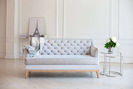 Modern Spacious minimalistic living room interior with a gray sofa and a coffee table with a vase with a bouquet of peonies flowers against a white wall. Scandinavian interior home. Cozy room decor.の写真素材