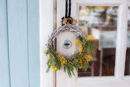 Front Door with wreath of Mimosa yellow flowers. Easter wreath. Spring decoration on wooden door of house. Home entrance with decorative Spring wreath on door. Rustic interior element of spring porchの写真素材