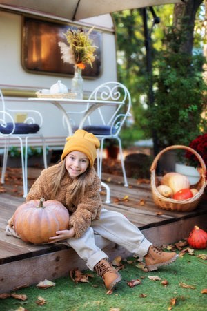 Happy little girl sitting on porch of house with pumpkins. home decorating for Halloween or...