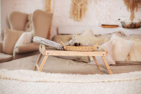 Bedroom interior with small table on bed with cones, christmas decorations. Wooden breakfast tray on bed in morning. Christmas room decor. Cozy New Year's composition. Cozy house interior on Xmas eve.の写真素材