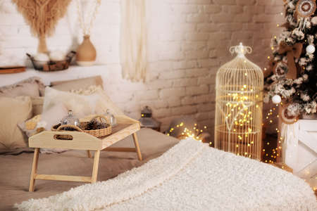 Wooden breakfast tray on bed in morning. Christmas room decor. Cozy New Year's composition. Cozy house interior on Xmas eve. Bedroom interior with small table on bed with cones, christmas decorations.の写真素材