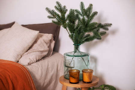 Branch fir tree at glass big vase. Cozy room decor for christmas with bed and vase with branches...