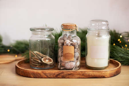 Glass jars with some aromatic spices and candle on an old wooden stand. Jar of dried sliced citrus fruits, Fir branch, Christmas spices and decor. Winter holidays, New Year or Christmas concept.の写真素材