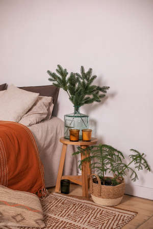 Modern room decor for christmas with bed and vase with branches pine on wooden table. Hygge Xmas decoration. Cozy rustic home. Scandinavian bedroom interior room. Basket with fir tree at living room.の写真素材