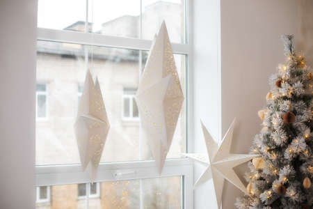 Hanging star lantern lights during holiday winter season. Decoration White Christmas stars in window. Advent time. A lamp in shape of star. Paper lightning lantern in star form. Star xmas paper lanterの写真素材