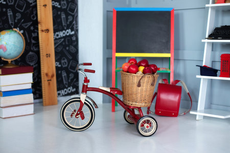 Red tricycle with basket apples. back to school. elementary school. Chalkboard, Books, globe in classroom.Empty classroom with blackboard. Kindergarten. Interior of children's roomの写真素材