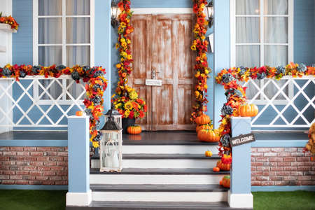House entrance staircase decorated for autumn holidays, fall flowers and pumpkins. Cozy wooden porch of the house with pumpkins in fall time. Halloween design home with yellow fallの写真素材
