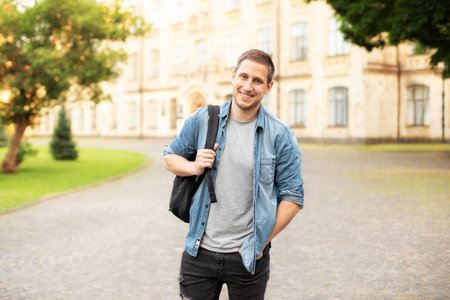 Successful student is standing with backpack near campus on the university background. Smiling young...