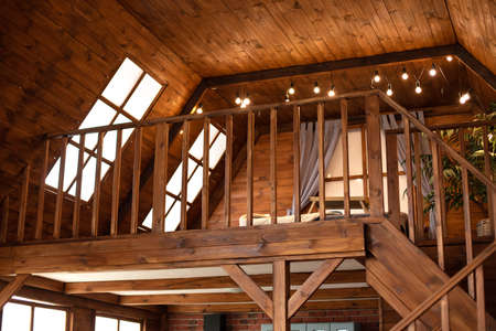 Wooden stairs in the attic of a country house with large windows.