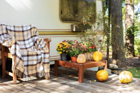 Wooden armchair near outside caravan trailer decorated for Halloween.Wooden RV house porch with garden furniture. Interior cozy yard campsite with fall flowers potted and pumpkins.の写真素材