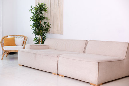 Modern beige sofa and wicker rattan armchair in wabi sabi loft interior with white wall. Elegant...