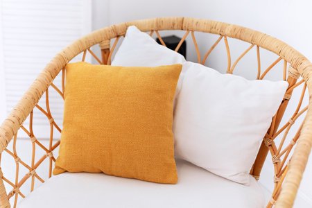 Design wicker wooden chair with pillows in stylish light bedroom interior. Rattan armchair by the white wall in the living room. Wabi sabi room interior. Eco natural furniture. Scandinavian style homeの写真素材