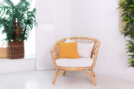 Design wicker chair in stylish light bedroom interior. Rattan armchair by the white wall in the...