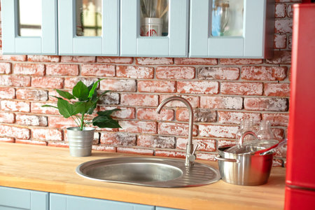 Facade of wooden blue kitchen in interior at home with modern furniture, cuisine sink and chrome faucet, utensils. Kitchen with cupboard and drawers and wooden countertop.の写真素材