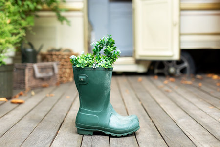 Green rubber boots with flowers and plants bouquet to contryyard. Cozy decor of autumn terrace of house. Garden boots. Rain boots in front of house on porch.の写真素材