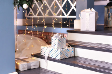 outdoor design home with Xmas tree and gifts in yard. House entrance staircase decorated for winters holidays, gifts, branches fir and glowing garland. porch of the house with giftの写真素材