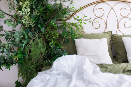 Comfortable bed with white pillows and green plants in the bedroomの写真素材