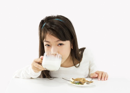 Cute girl drinking a glass of milk and eating a cakeの写真素材