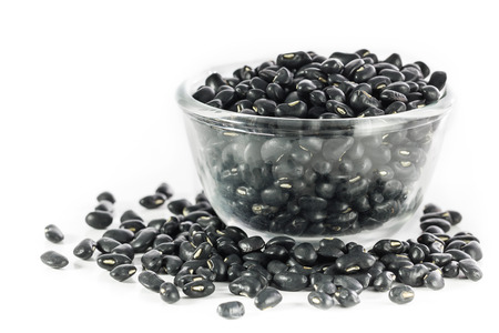 Glass bowl full  of dry black beans on white background