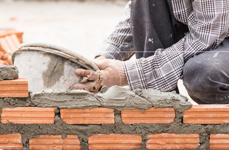 Bricklayer working in construction site of a brick wall. Bricklayer putting down another row of bricks in siteの写真素材