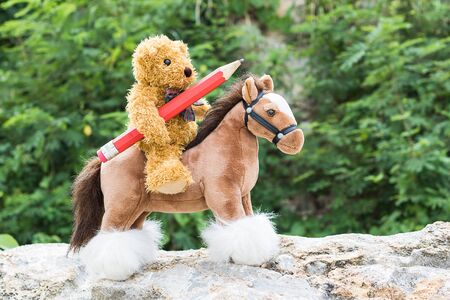 Teddy bear ride a horse and hold pencil in forestの写真素材