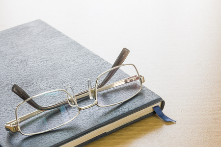 Glasses put on a text book on wood desk backgroundの写真素材