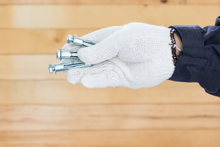 Working hand in glove holding metal anchor bolts with wall wood backgroundの写真素材