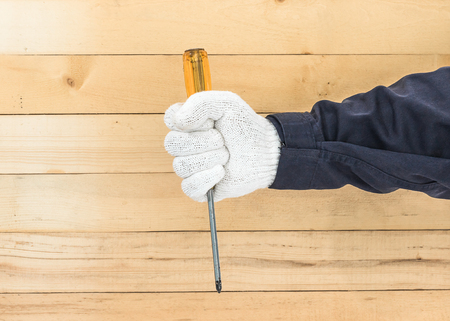 Working hand in glove holding screwdriver with wall wood backgroundの写真素材