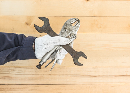 Working hand in glove holding a Spanner and Adjustable wrench with wall wood background