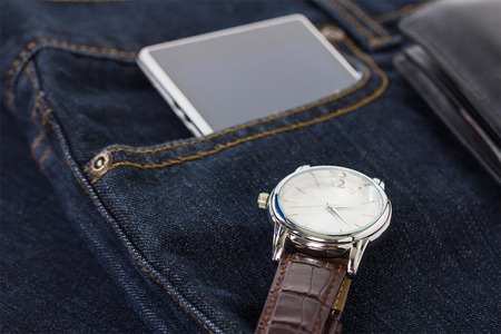 Top view of wrist watch on brown leather strap and smartphone on denim jeans pocketの写真素材