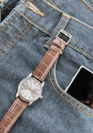 Top view of wrist watch on brown leather strap and smartphone on jeans pocketの写真素材