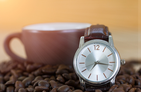 Coffee time concept ,Close up of roasted brown coffee beans on wood tray and wrist watch with coffee cupの写真素材