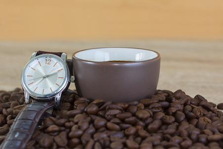 Coffee time concept ,Close up of roasted brown coffee beans on wood tray and wristwatch with coffee cupの写真素材