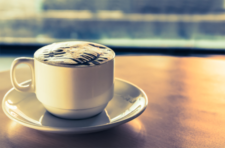 Close up white coffee cup with art foam on  wood table on tabletop at cafeの写真素材