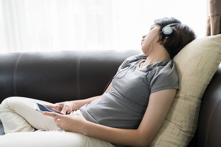 Close up beautiful young asian woman short hair listening music on the couch at homeの写真素材