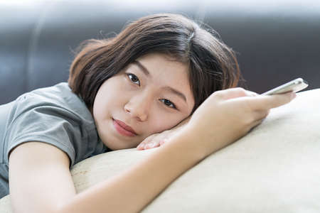 Close up young asian woman short hair listening music from mobile phone on the couch at homeの写真素材