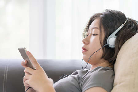 Close up young asian woman short hair listening music from mobile phone on the couch at home