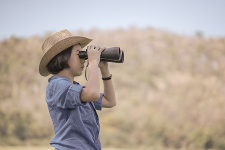 Young asian woman short hair wear hat and hold binocular in grass field countryside Thailandの写真素材